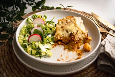 Ein Teller mit Kartoffel Linsen Auflauf serviert mit grünem Salat mit Radieschen auf einem weißen Teller
