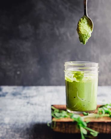 Grünes Pesto aus Microgreens das von einem Löffel in ein Glas tropft.