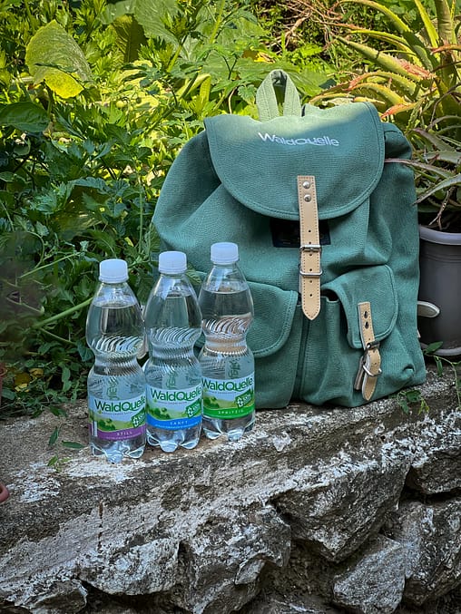 Waldquelle Wanderrucksack mit drei Flaschen Mineralwasser, gepackt fürs den Wandertag und zum Grillen von Steckerlbrot.
