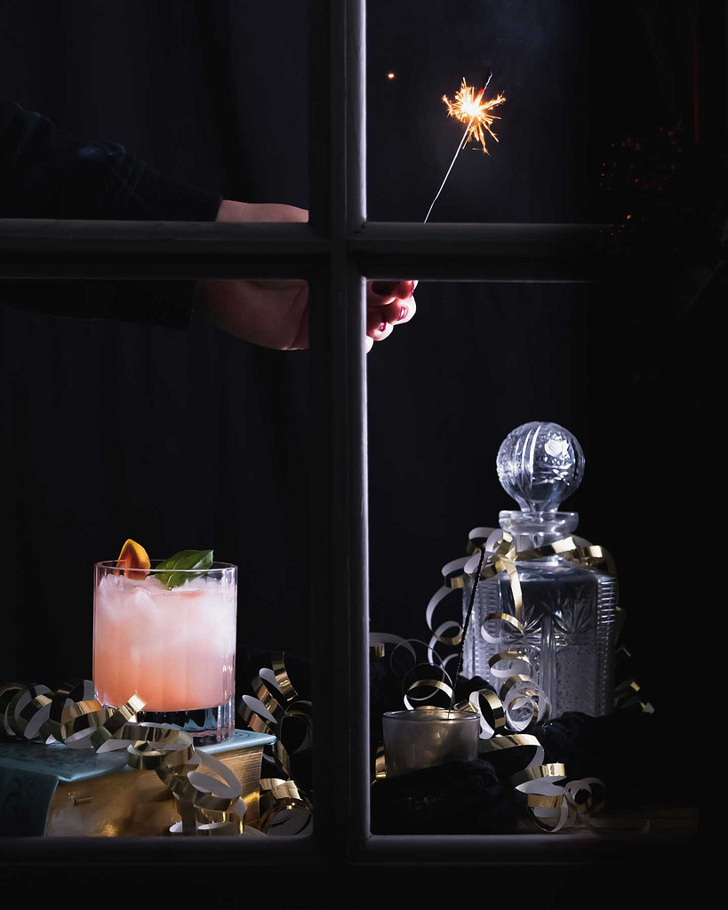 Ein Glas Grapefruit Gin Tonic durch ein Fenster fotografiert. Eine Person hält einen Sternderlwerfer.